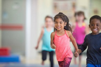 A multi-ethnic group of elementary age children are running to warm up during a gymnastics class together at the gym.
