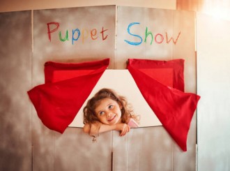 Shot of an adorable little girl standing in the window of a puppet show theatre at home